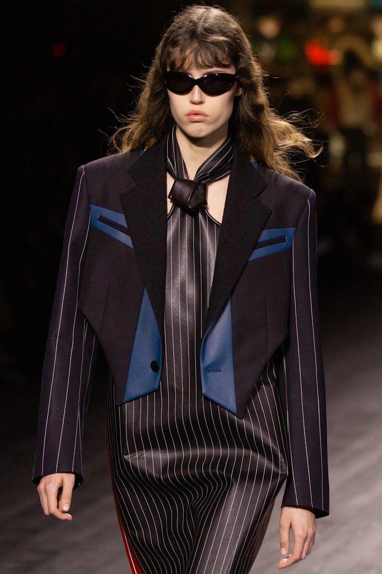A model walking in a black-white striped dress and a black-blue blazer at the Louis Vuitton fall 202...