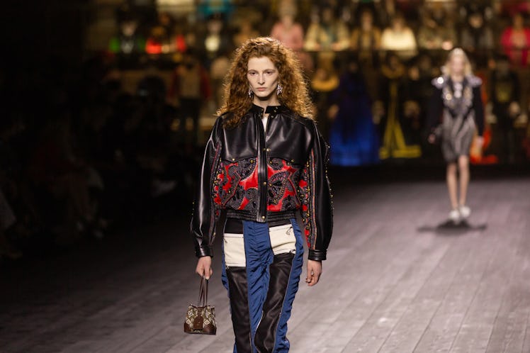 A model walking in a black-red jacket and black-white-blue trousers at the Louis Vuitton fall 2020 s...