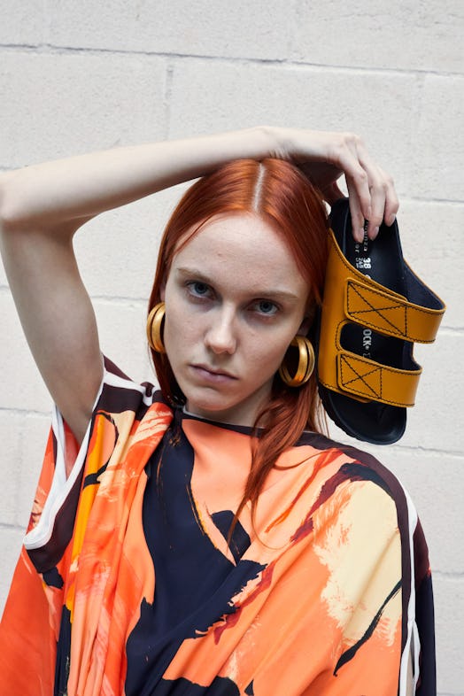 Ginger haired model holding a Birkenstock yellow slipper beside her head