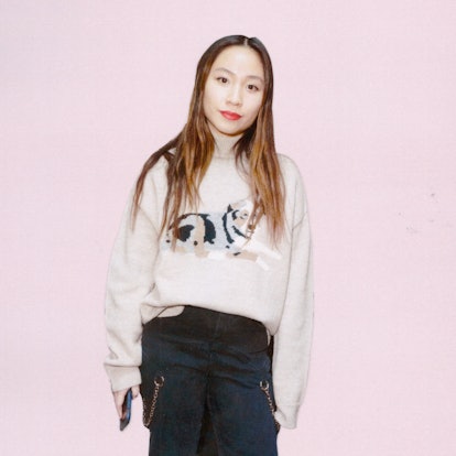 A portrait of Sandy Liang in a white sweater with a dog print and blue denim jeans