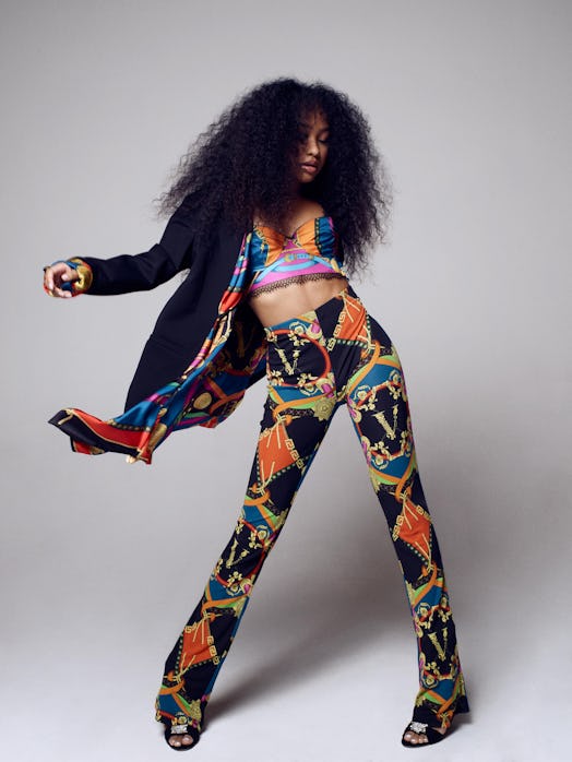 Genneya Walton posing while wearing a black, orange, gold, and blue cardigan, top, and multi-colored...