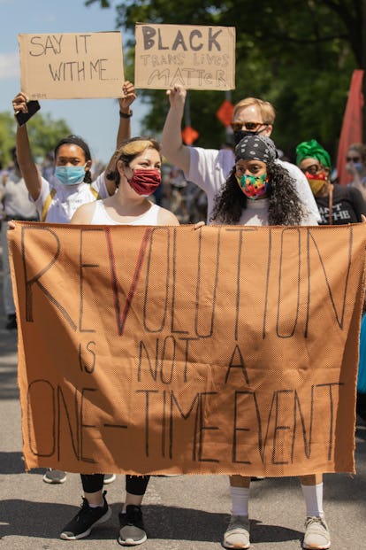 Women holding signs against racism at the #BlackLivesMatter protests with a large 'Revolution is not...