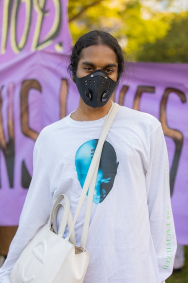 A woman posing in a white shirt while wearing a black face mask