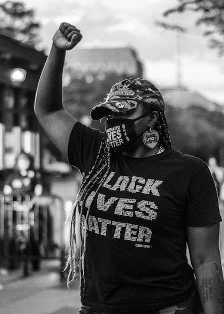 A woman with braid with her arm raised in a shirt with the text 'Black Lives Matter' at a protest