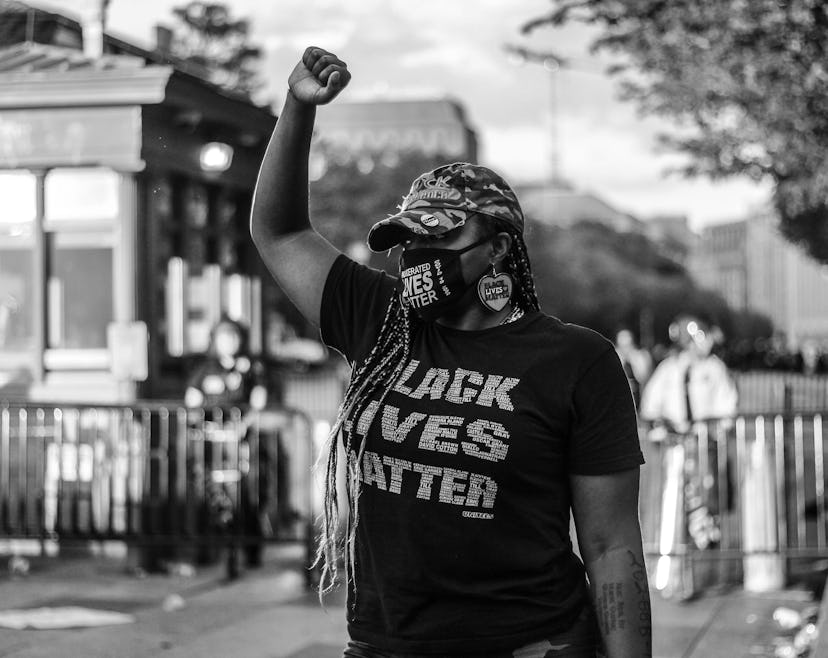A woman with braid with her arm raised in a shirt with the text 'Black Lives Matter' at a protest