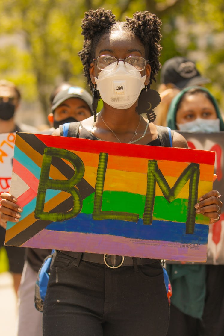 A woman in a black top and trousers holding an LGBTQ+ painted BLM protest sign