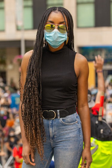 A woman in a black top, blue denim jeans, a blue face mask and yellow sunglasses on the 4th of July