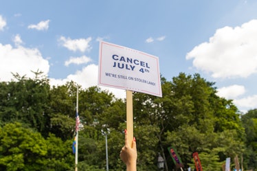 A person holding a white sign with the text 'Cancel July4th' on the 4th of July