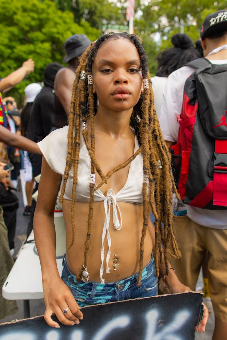 A woman in a white tied crop top and blue denim jeans holding a black lives matter sign