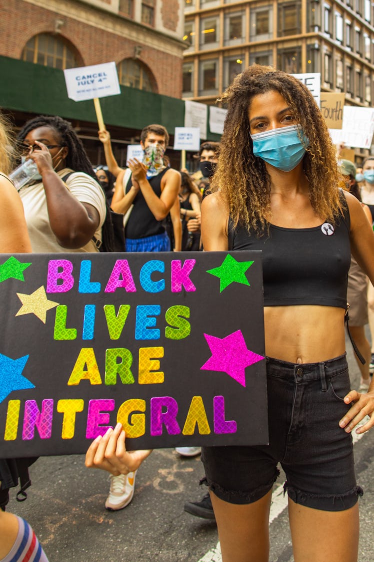 A woman in a black top and shorts holding a black sign with the text 'BLACK LIVES ARE INTEGRAL' on t...