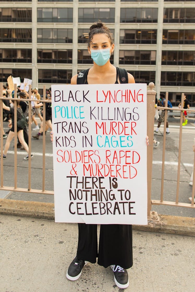 A woman holding a poster with a text with BLM issues, wearing a blue face mask on the 4th of July