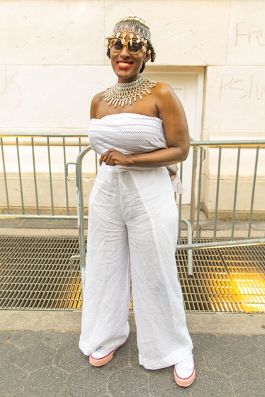 A woman in a white jumpsuit, statement necklace and head piece smiling on the 4th of July