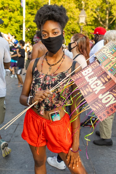 A woman in a black floral top, orange shorts and a black face mask holding a 'Black Joy' sign on the...