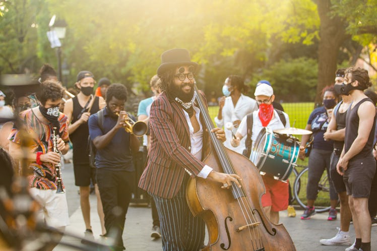 A man playing on a double bass in a striped suit and people standing around him on the 4th of July