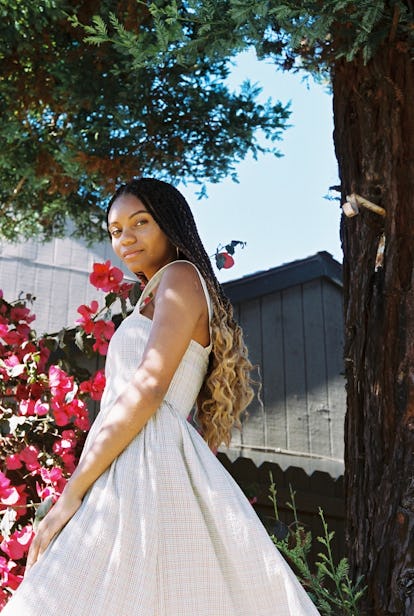 Green girl Leah Thomas posing in a white sundress among pink flowers