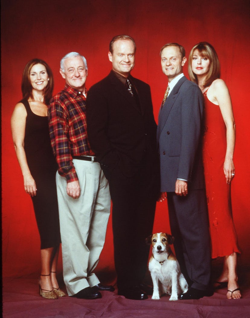 The cast of Frasier posing with a dog against a red backdrop 