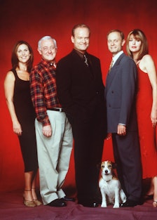 The cast of Frasier posing with a dog against a red backdrop 