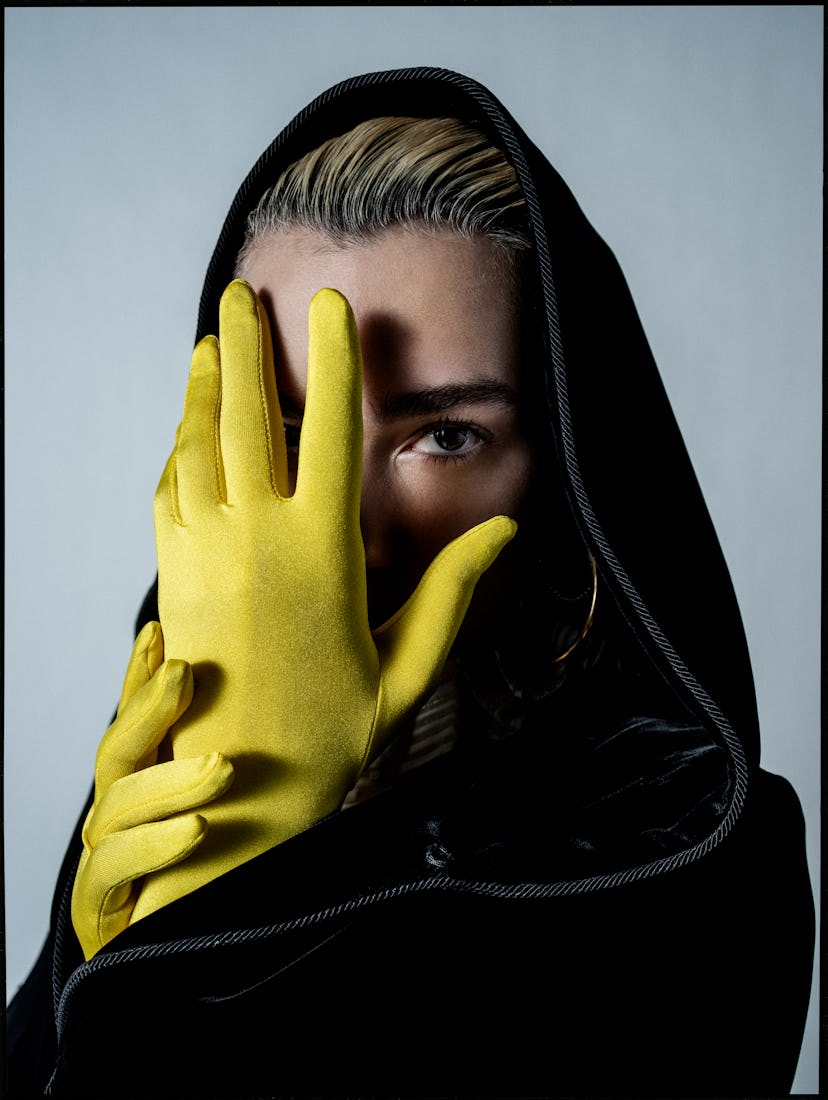 A woman in a black cloak covering her face with her hands, which are in yellow gloves