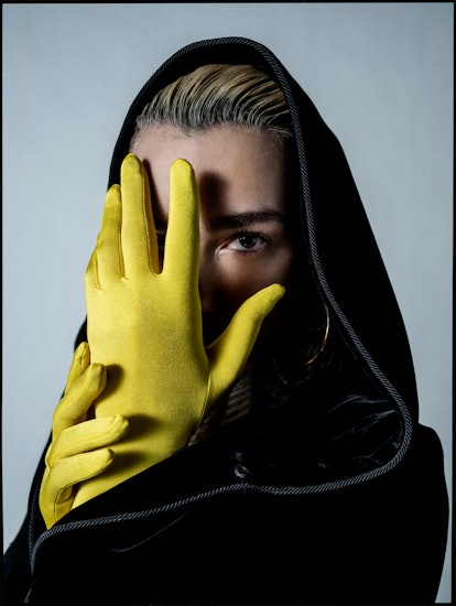 A woman in a black cloak covering her face with her hands, which are in yellow gloves