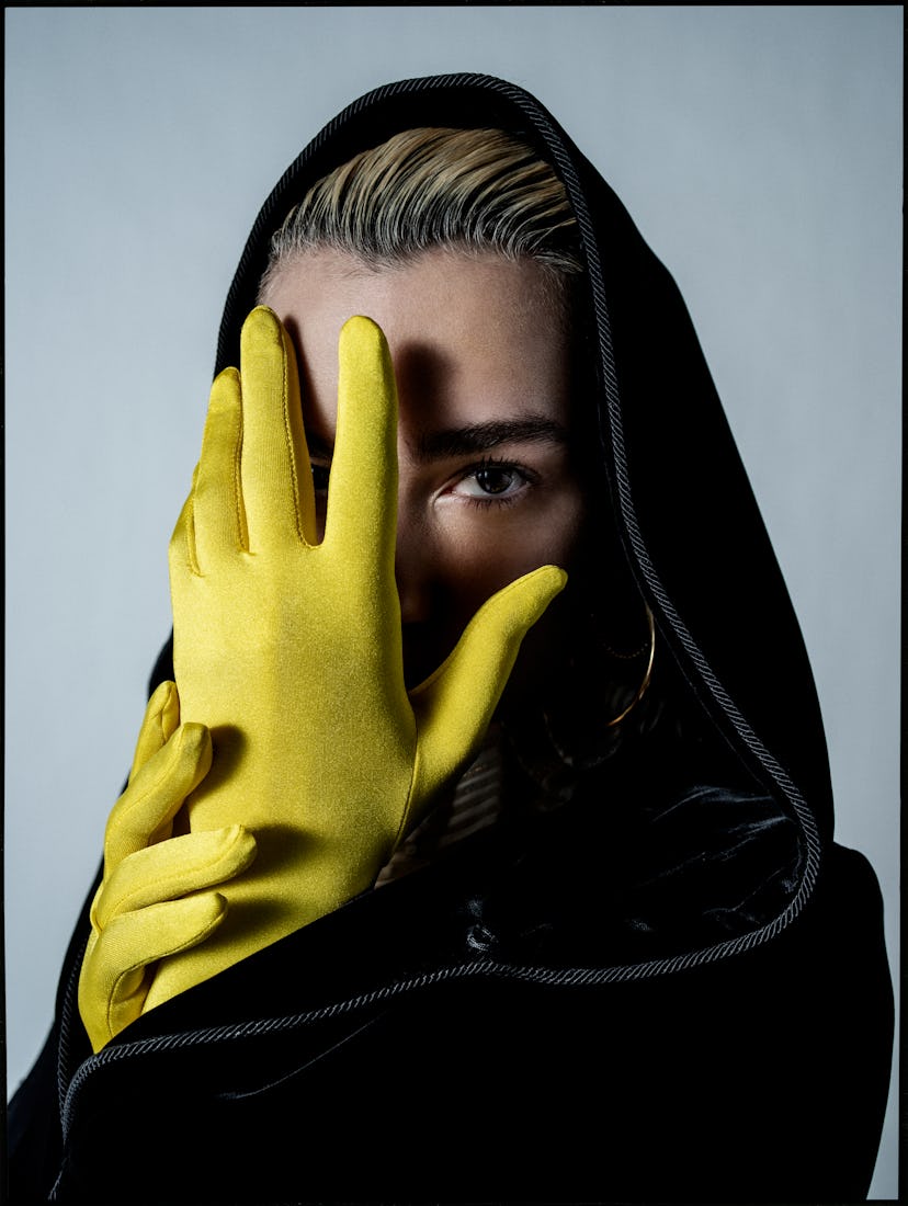 A woman in a black cloak covering her face with her hands, which are in yellow gloves