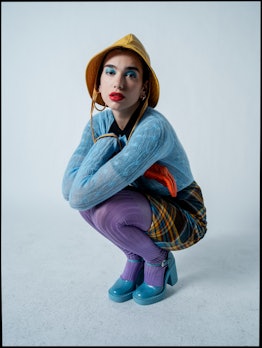 Dua Lipa posing in a blue Prada sweater, plaid skirt, purple tights, and Maison Margiela Artisanal D...