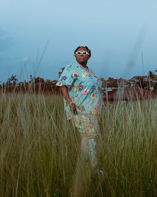 Teniola Apata posing in a grass field while wearing a light blue shirt
