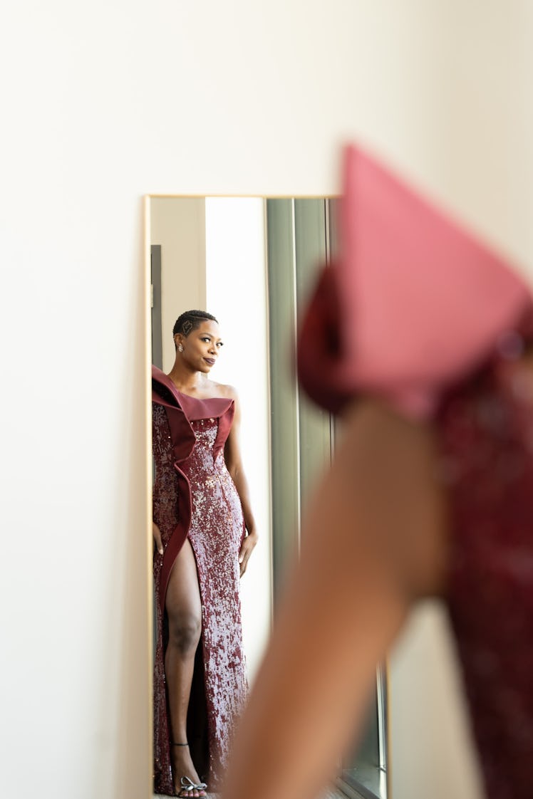 Yvonne Orji looking herself in the mirror while wearing a red gown 