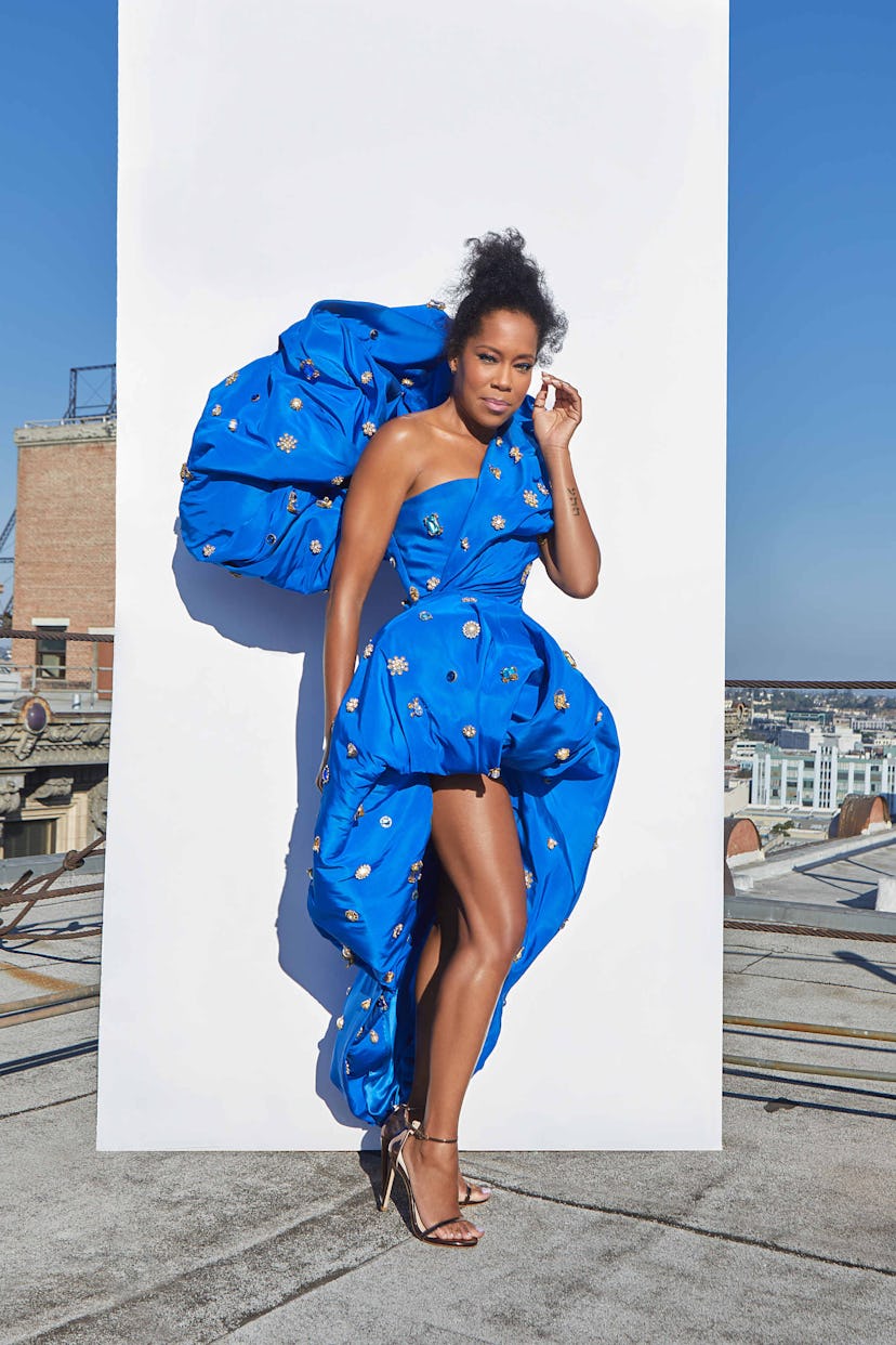 Regina King in a blue Schiaparelli dress with silver details posing next to a white wall