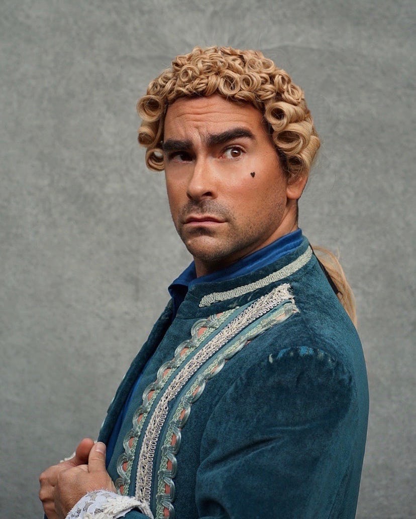 A portrait of Dan Levy in a blonde judge wig, and a teal blazer with embroidery