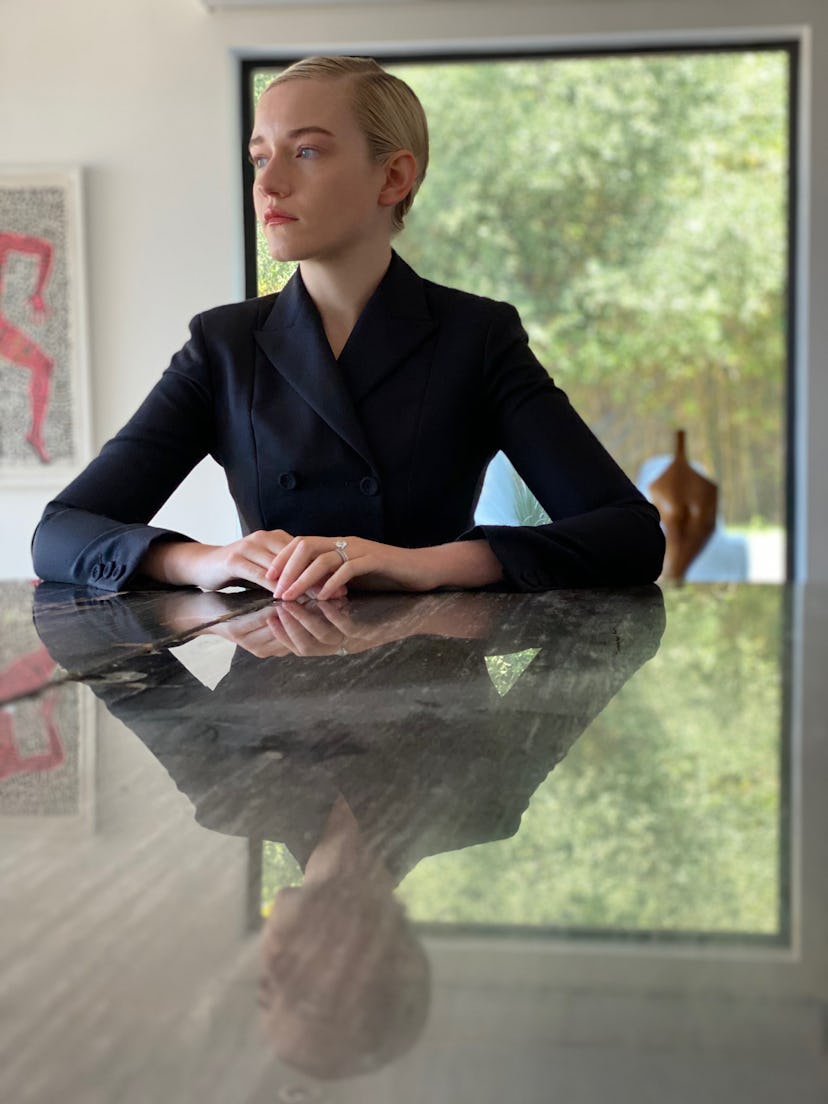 Julia Garner in a black blazer sitting at a table with a large window in the background
