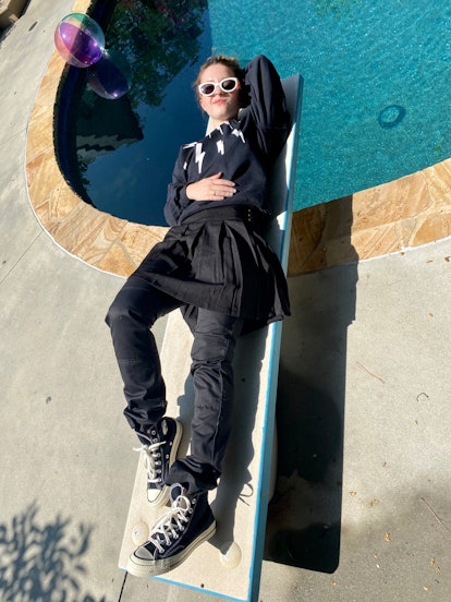 Kaitlyn Dever dressed as David Rose from Schitt's Creek lying on a sunbed next to a pool 