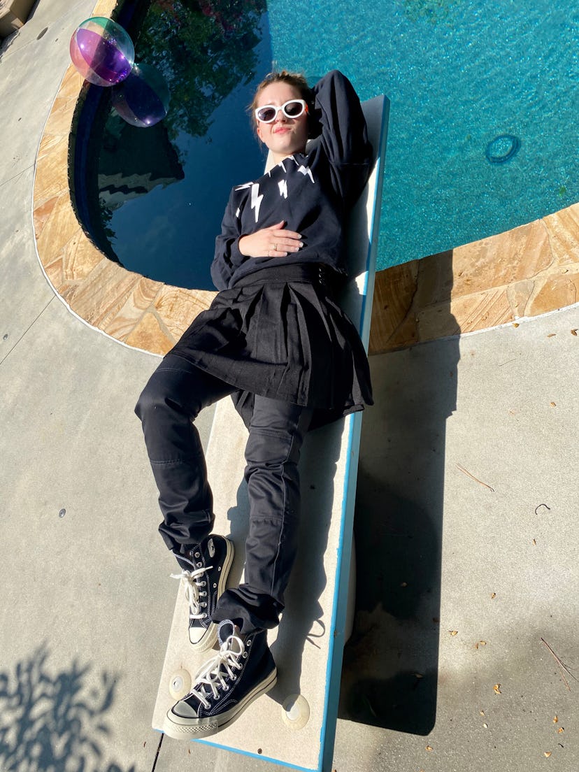 Kaitlyn Dever dressed as David Rose from Schitt's Creek lying on a sunbed next to a pool