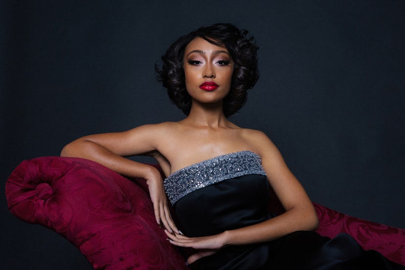 Lexi Underwood on a red velvet couch in a black strapless gown with a shimmery boarder on top 