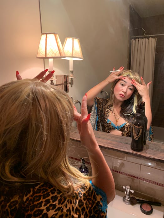 Maya Erskine checking looking at herself in a mirror while wearing a brunette wig