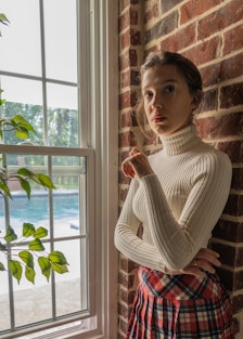 Millie Bobby Brown dressed as Rachel from Friends in a white turtleneck and plaid skirt