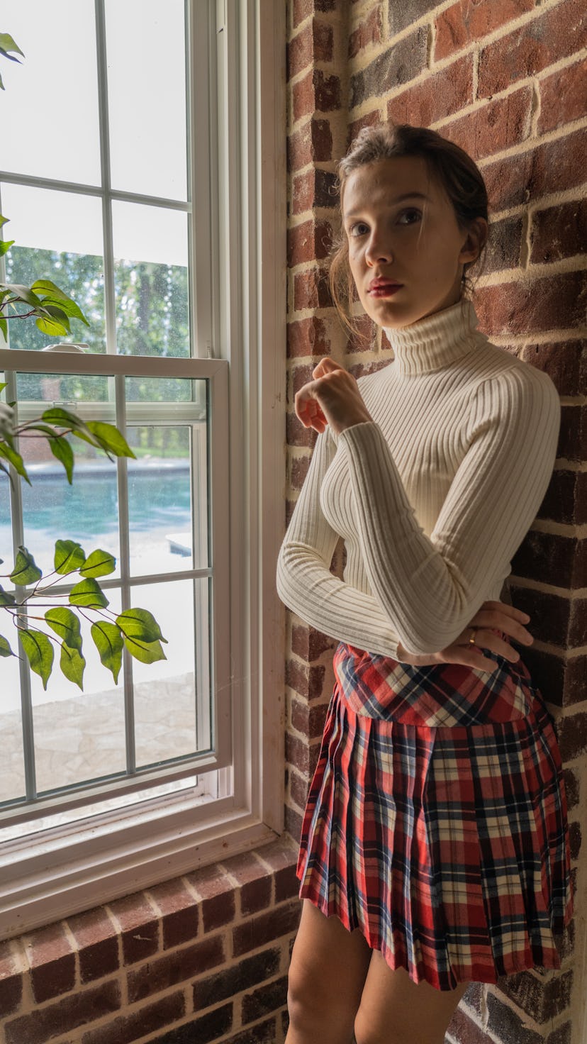 Millie Bobby Brown dressed as Rachel from Friends in a white turtleneck and plaid skirt