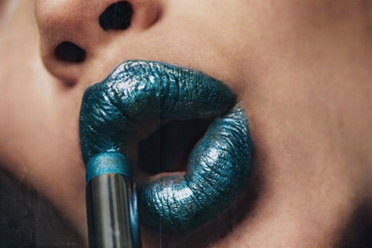 A woman applying teal Byredo Makeup Colour Sticks on her lips