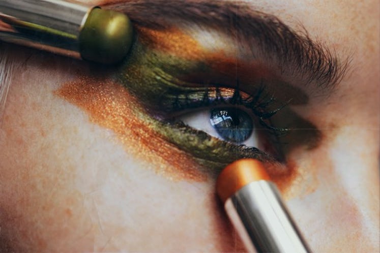 A woman applying green and orange Byredo Makeup Colour Sticks on her eyelids and around them