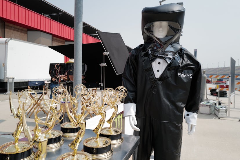 A mannequin dressed in a hazmat suit and Emmy award statues on a table