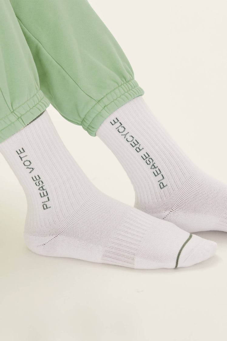 A model sporting green sweat pants and Girlfriend Collective Socks in white with black text print
