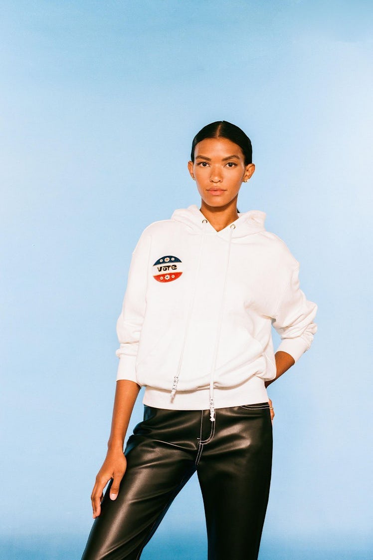 A model sporting black leather trousers and a white Staud Hooded Sweatshirt