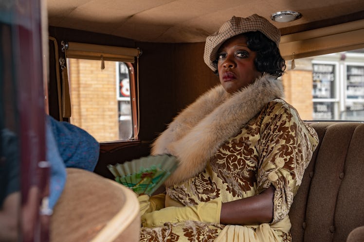 Viola Davis sitting in a yellow floral dress, beige scarf and hat and yellow gloves in Ma Rainey’s B...