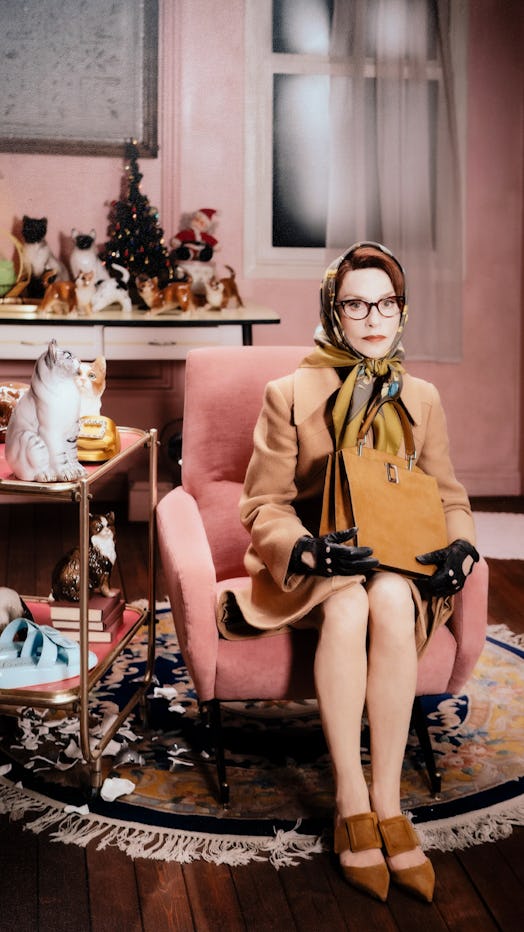 Isabelle Huppert sitting with a scarf over her head