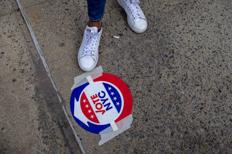 Feet in white sneakers next to a "Vote NYC" sticker on the ground 