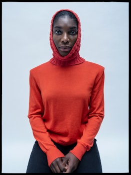 Michaela Coel wearing a red sweater, a red knitted hat, and black pants