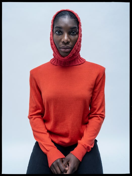 Michaela Coel wearing a red sweater, a red knitted hat, and black pants