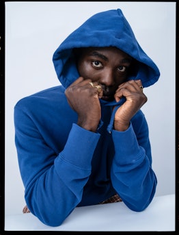 Paapa Essiedu in a blue hoodie and brown, red, and white checkered pants