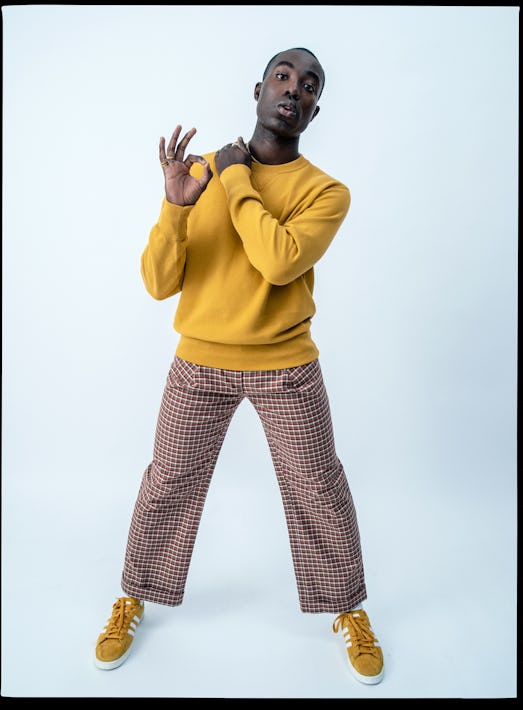 Paapa Essiedu in a yellow sweater, brown, red, and white checkered pants, and Adidas sneakers