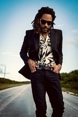 Lenny Kravitz wearing a Saint Laurent jacket, shirt, jeans, and sunglasses while posing for a photo