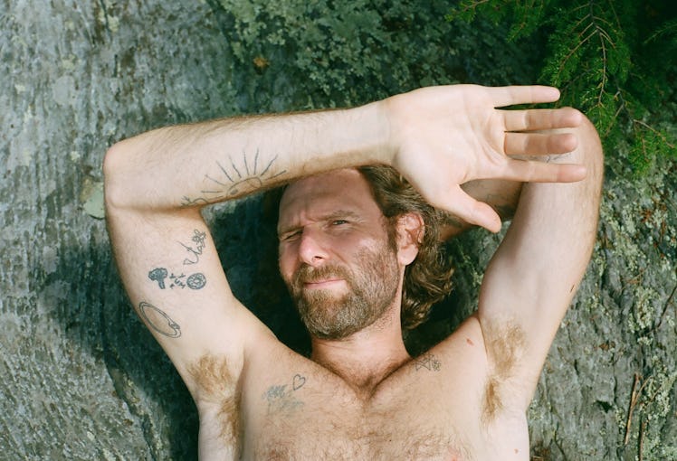 A shirtless Dan Colen posing for a photo while lying on the ground